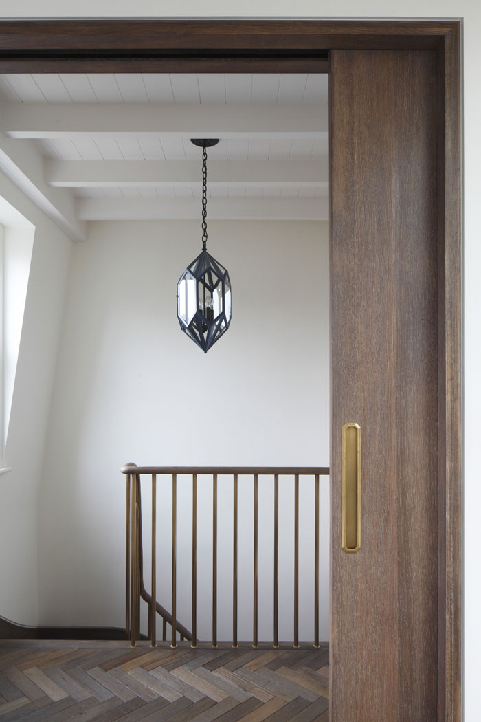 Large pocket door in fumed oak finish. Beamed ceiling and herringbone floor, with brass balustrade and oak handrail. Urban Electric Diamond pendant fitting over staircase.