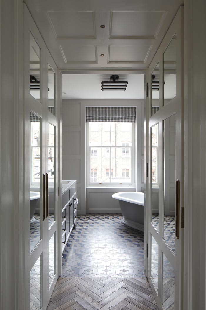 Panelled entrance to master bathroom, showing reclaimed herringbone floor and stone mosaic floor in bathroom. Apparatus studio ceiling light fitting