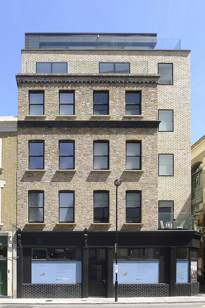 New historic brick facade, with glazed brick shop front and historic timber detailing. Modern brick facade set back differentiates between restored old and new in the Shoreditch Conservation Area.