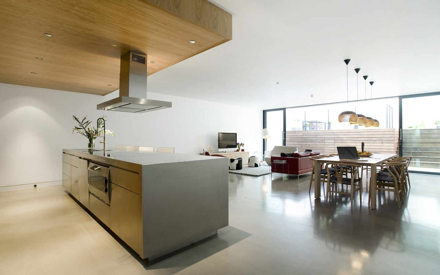 Family room with polished concrete floor, stainless steel island unit, oak kitchen wall units, oak dining table.