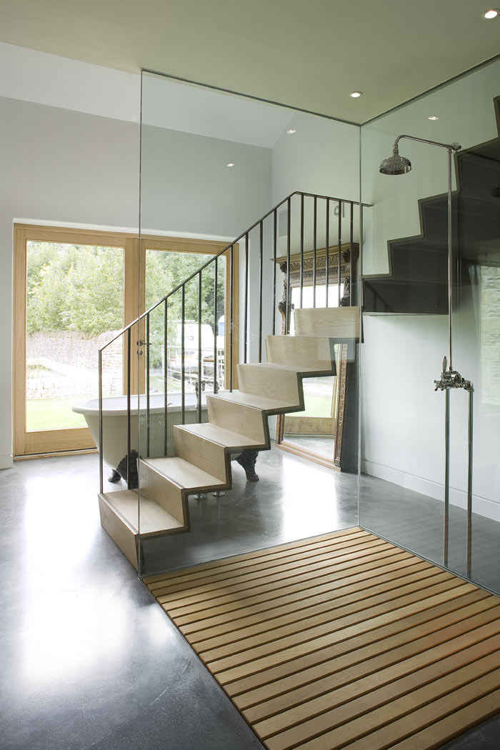 Master bathroom with folded metal staircase and roll top bath. Polished concrete floor and original stone walls. Screened shower area, with recessed oak floor.