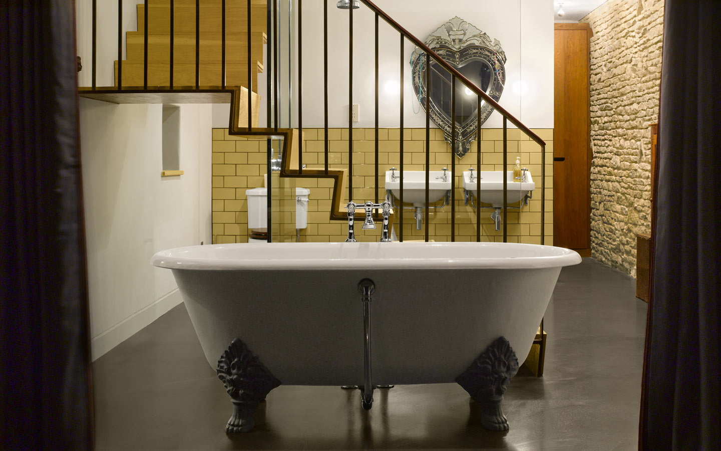 Master bathroom with folded metal staircase and roll top bath. Polished concrete floor and original stone walls.