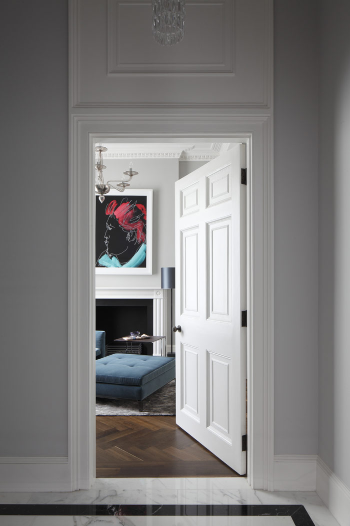Refurbished original panelled door into room with herringbone floor, Murano glass chandelier, Chesneys stone heritage fireplace, Minotti furniture and Malec Fustok print. 