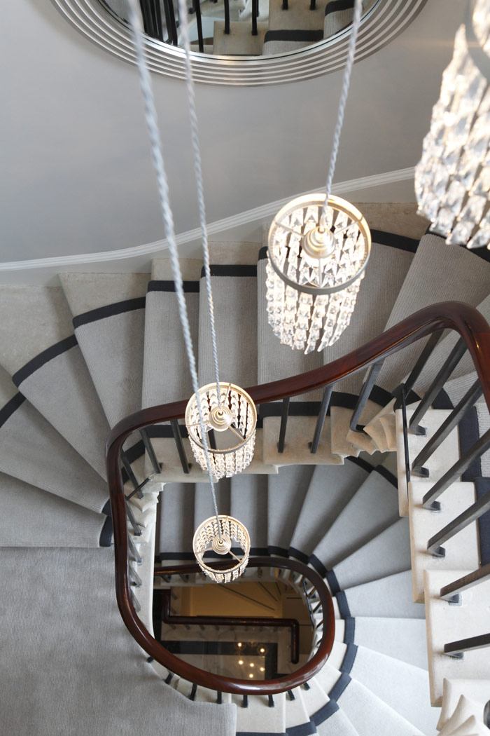 Refurbished original cantilevered stone staircase, showing carpet runner and crystal chandelier.