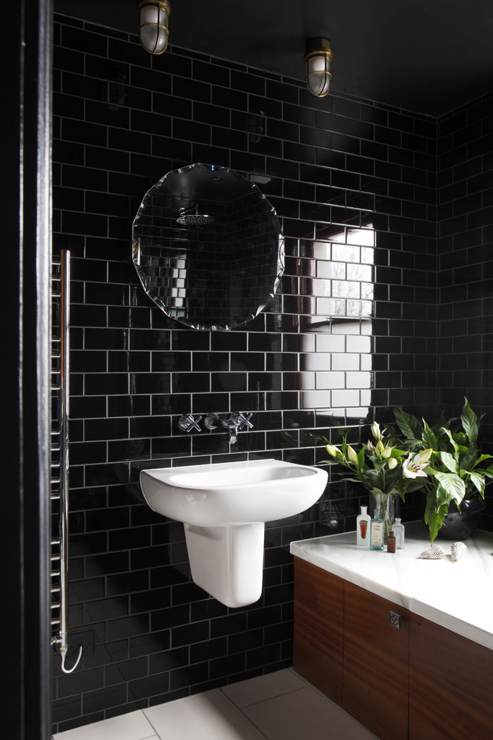 Black bathroom, with glazed brick format tiles, Sapele timber lined bath, antique mirror and reclaimed ceiling lights.