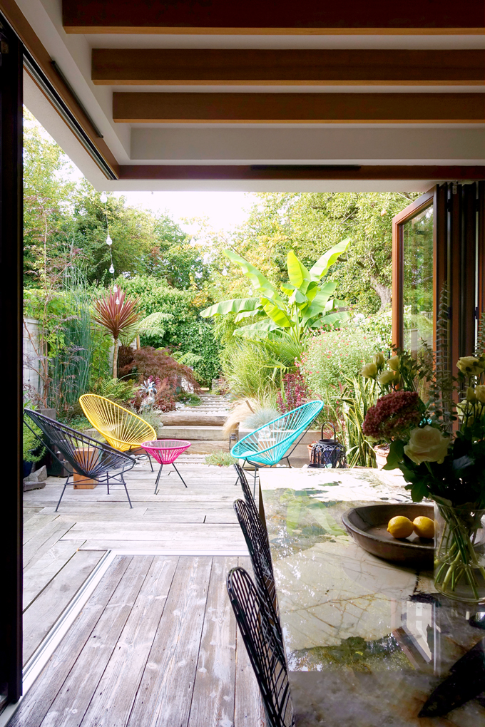 Rear ground floor extension with floor to ceiling bifolding doors, exposed beams and level threshold detail. Timber sleepers used for external landscaping, tropical planted garden and Acapulco chairs and table.
